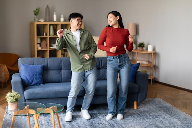 Giovani coniugi asiatici amorevoli che ballano insieme a casa facendo festa