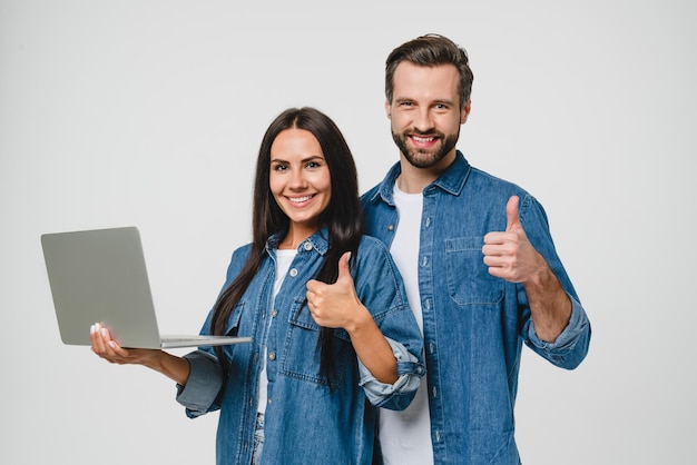 Giovani coppia caucasica coniugi amici uomo e donna con laptop per l'e-learning e-commerce lavoro a distanza guardando webinar mostrando il pollice in alto isolati sullo sfondo bianco