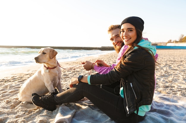 Giovani coppie adorabili che giocano con il loro cane in spiaggia