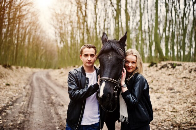 Giovani coppie alla moda nell'amore vicino al cavallo alla foresta di autunno