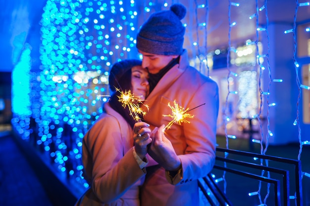 Giovani coppie amorose che bruciano stelle filanti dall'illuminazione delle vacanze. Concetto di Natale e Capodanno