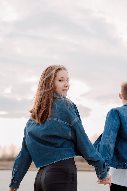 Giovani coppie amorose che indossano jeans che trascorrono del tempo insieme nel parco divertendosi, donna che si tiene per mano con il suo ragazzo che guarda indietro