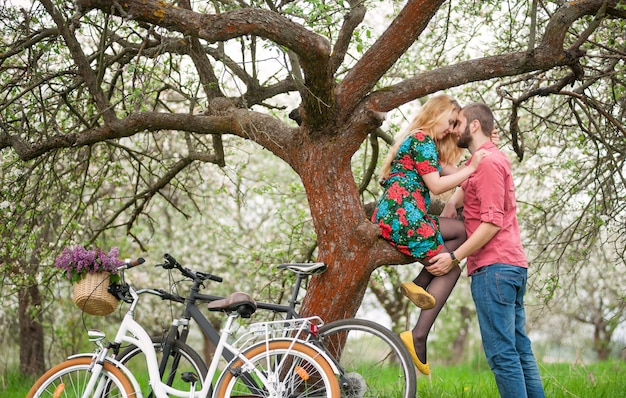 Giovani coppie amorose con le biciclette nel giardino di primavera