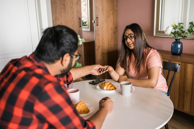 Giovani coppie amorose diverse che mangiano croissant e parlano insieme a casa durante la colazione Concetto di comunicazione e relazione