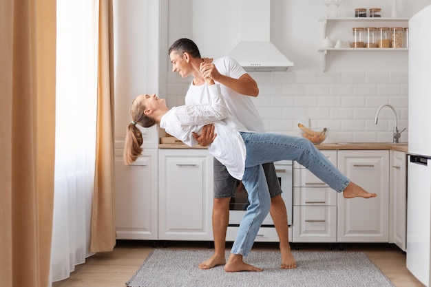 Giovani coppie amorose felici che ballano alla data nella cucina moderna marito e moglie sorridenti che celebrano l'anniversario godendosi un momento tenero divertendosi