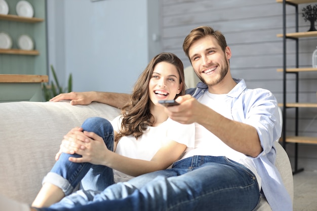 Giovani coppie amorose sul divano di casa a guardare la tv e ridere.