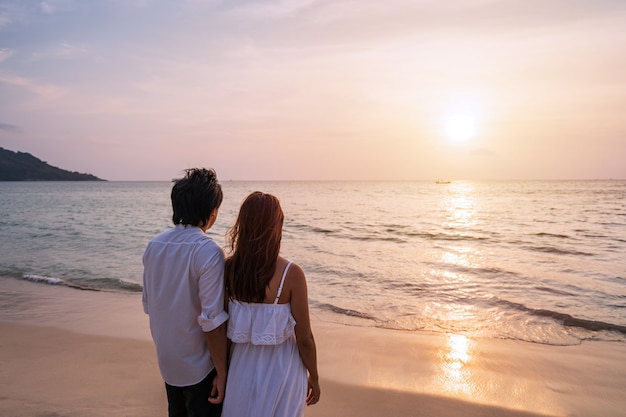 Giovani coppie asiatiche che sembrano bello tramonto sulla spiaggia