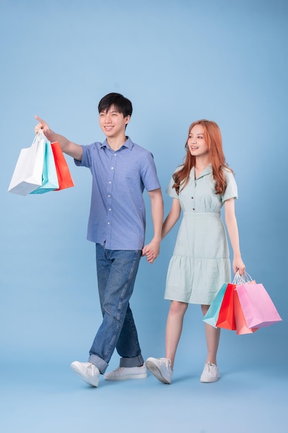 Giovani coppie asiatiche che trasportano la borsa della spesa su sfondo blu