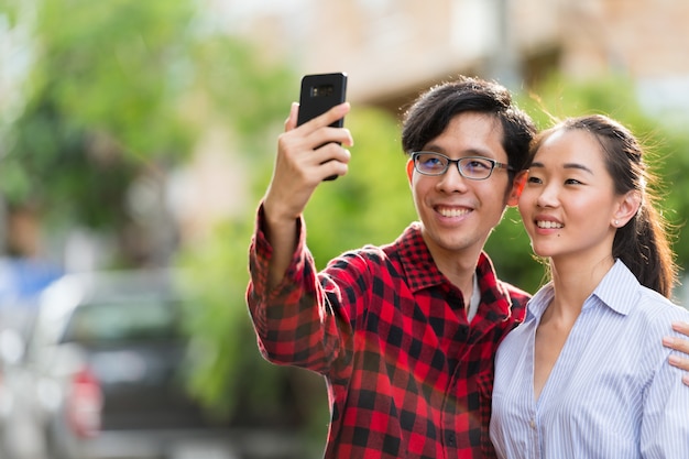 Giovani coppie asiatiche felici che prendono selfie insieme all'aperto