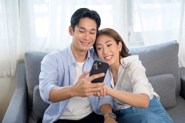 Giovani coppie asiatiche sorridenti che utilizzano smartphone nel soggiorno di casa