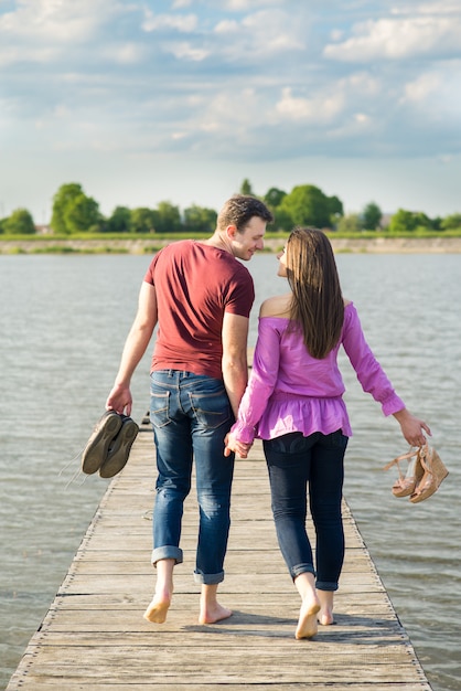 Giovani coppie che camminano a piedi nudi dal ponte di legno sul lago