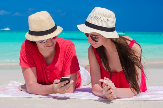 Giovani coppie che esaminano telefono che si trova sulla spiaggia tropicale