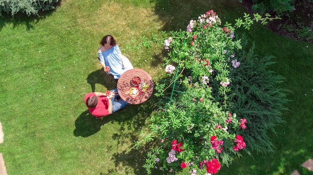 Giovani coppie che godono del cibo e del vino nel bellissimo giardino di rose alla data romantica, vista aerea dall'alto dall'alto di uomo e donna, mangiare e bere insieme all'aperto nel parco