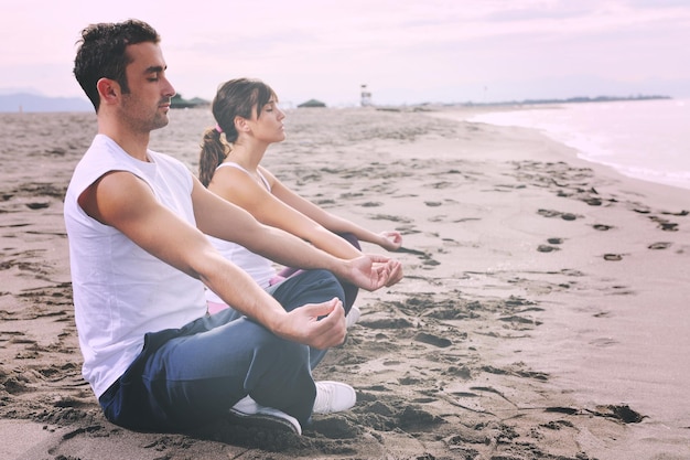 giovani coppie che meditano yoga nella posizione del loto al mattino presto sulla spiaggia