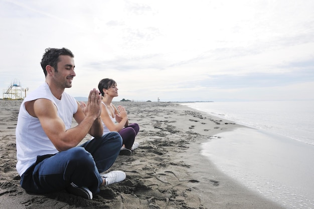 giovani coppie che meditano yoga nella posizione del loto al mattino presto sulla spiaggia