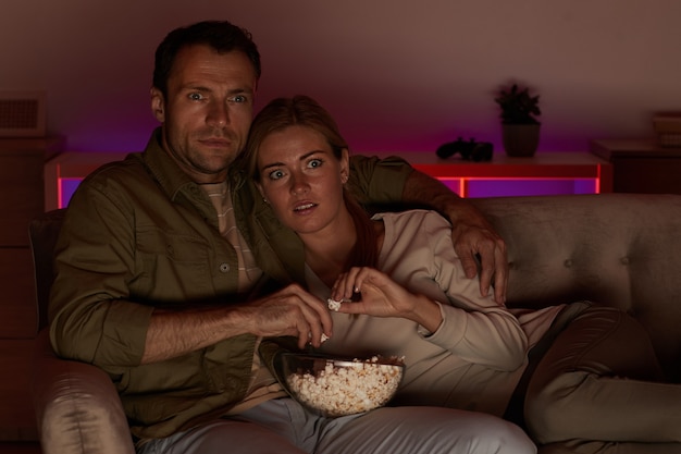 Giovani coppie che sembrano molto spaventate si sdraiano sul divano con popcorn e guardano film spaventosi