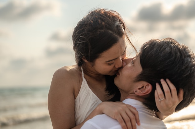 Giovani coppie che si abbracciano e si baciano sulla spiaggia al tramonto. Estate in amore, concetto di San Valentino.