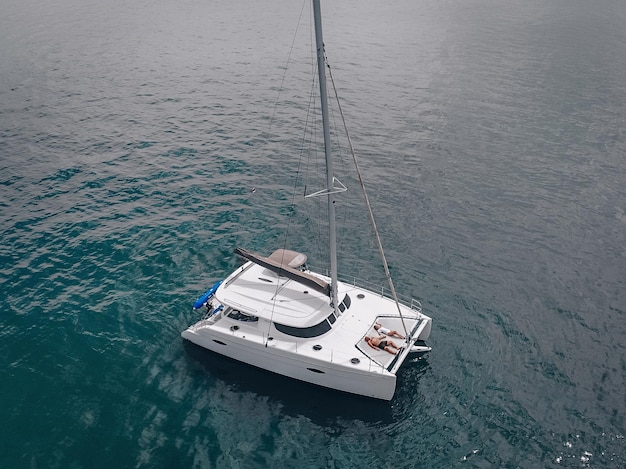 Giovani coppie che si rilassano a bordo della barca a vela ancorata nella baia tropicale poco profonda. Foto aerea