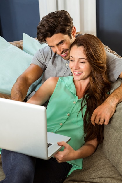 Giovani coppie che si siedono sul sofà e che per mezzo del computer portatile