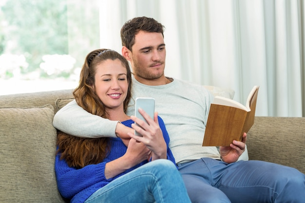 Giovani coppie che si siedono sul sofà e sul telefono cellulare in salone