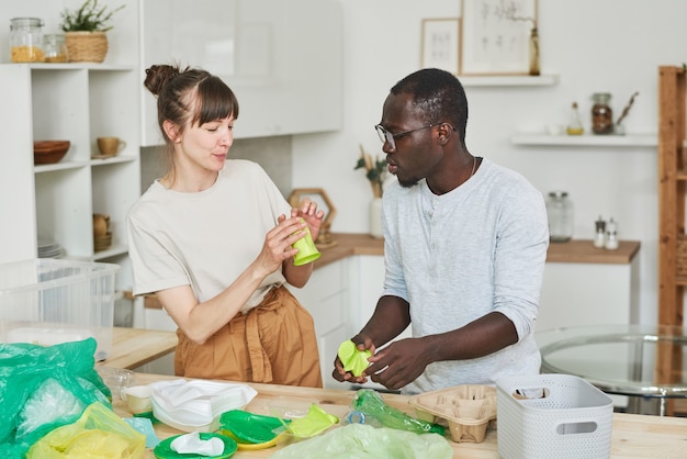 Giovani coppie che smistano la spazzatura insieme nella cucina di casa