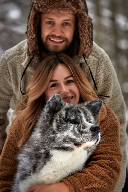 Giovani coppie che sorridono e si divertono nel parco invernale con il loro cane husky