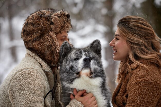 Giovani coppie che sorridono e si divertono nel parco invernale con il loro cane husky