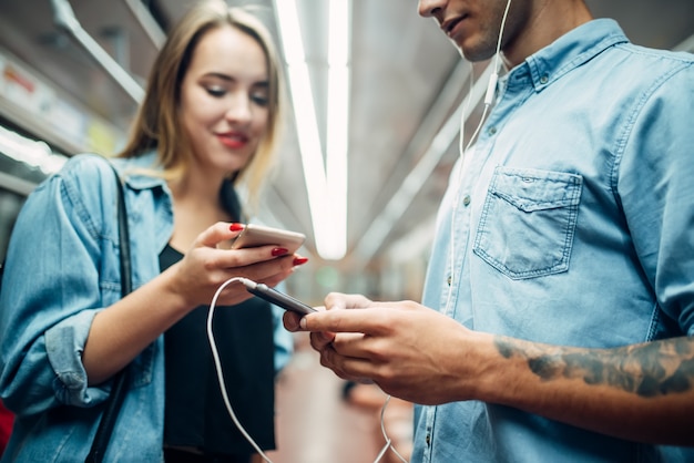 Giovani coppie che utilizzano i telefoni in vagone della metropolitana, problema di dipendenza, persone dipendenti dalla società, moderno stile di vita sotterraneo