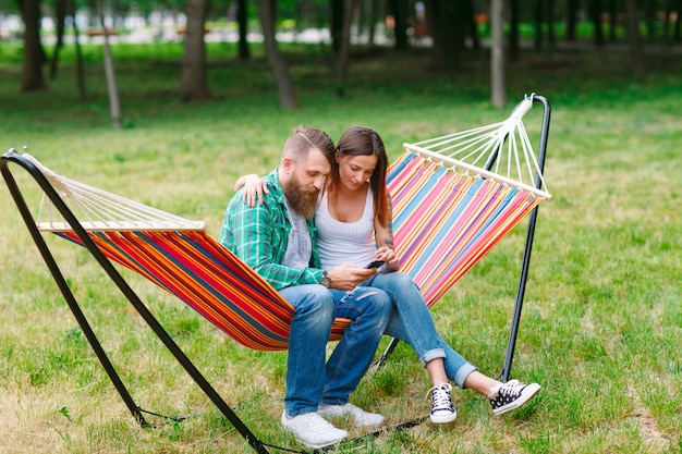 Giovani coppie con il telefono cellulare che si siede sull'amaca