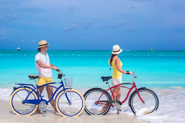 Giovani coppie con le bici sulla spiaggia sabbiosa bianca