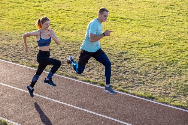 Giovani coppie degli sportivi adatti ragazzo e ragazza che corrono mentre facendo esercizio sulle piste rosse dello stadio pubblico all'aperto.