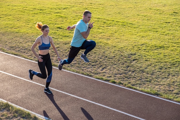 Giovani coppie degli sportivi adatti ragazzo e ragazza che corrono sulle piste rosse dello stadio pubblico