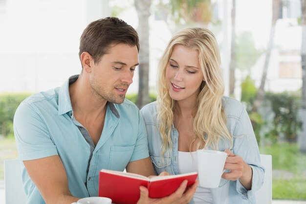 Giovani coppie dell&#39;anca che mangiano insieme libro di lettura del caffè