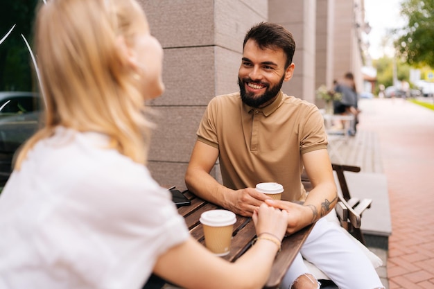 Giovani coppie di incontri sorridenti felici che mangiano caffè insieme e si godono la vita seduti al tavolo tenendosi per mano in un caffè di strada il giorno d'estate
