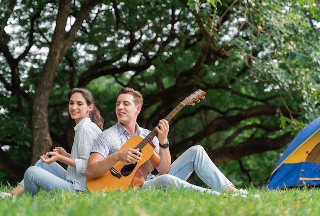 Giovani coppie divertendosi con la chitarra sul picnic e accampandosi nel parco