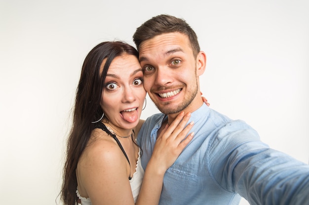 Giovani coppie divertenti attraenti che prendono selfie insieme su fondo bianco