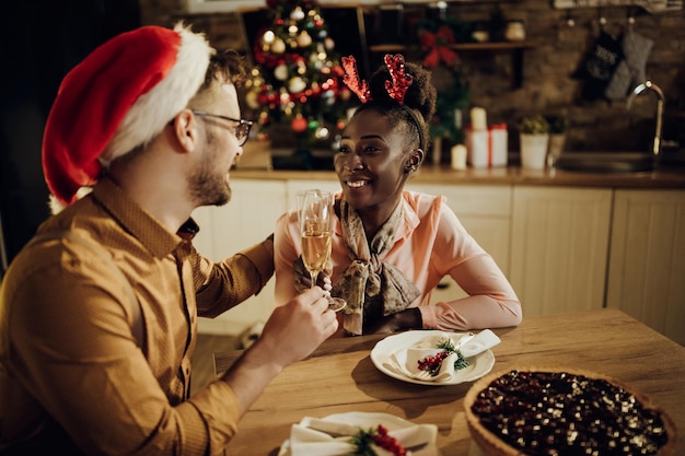 Giovani coppie felici che brindano al tavolo da pranzo la vigilia di Natale a casa