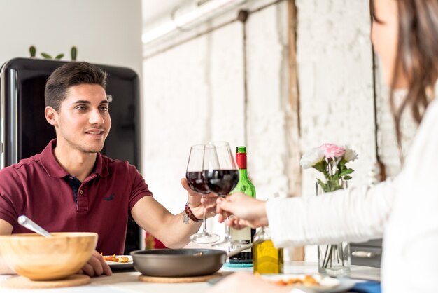 Giovani coppie felici che mangiano e che bevono vino a casa