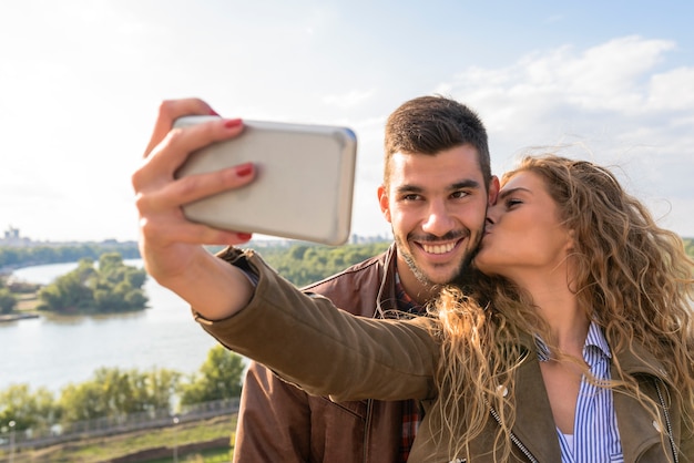 Giovani coppie felici che prendono le foto del selfie vicino al fiume