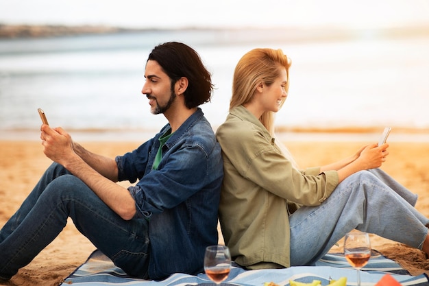 Giovani coppie felici che si rilassano con gli smartphone sulla spiaggia all'aperto
