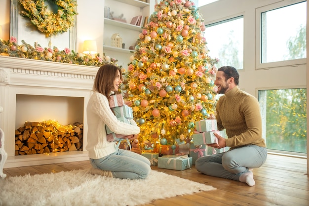 Giovani coppie felici che si siedono vicino all'albero di Natale