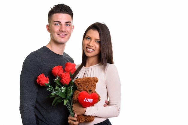 Giovani coppie felici che sorridono mentre si tengono rose rosse e orsacchiotto