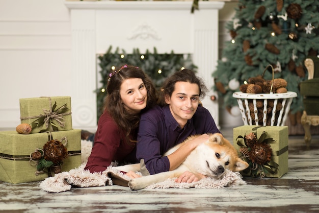 Giovani coppie felici che stringono a sé il cane adorabile di inu di akita con sul pavimento per le feste di Natale a casa.