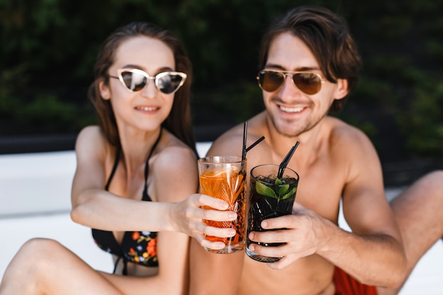 Giovani coppie felici con le bevande che si rilassano sulla spiaggia