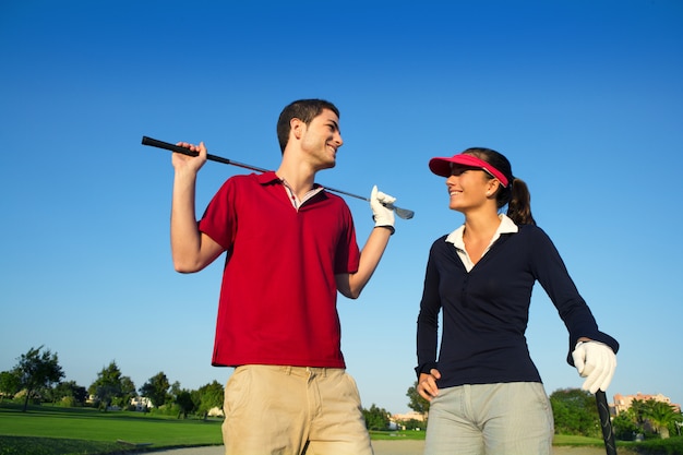 Giovani coppie felici dei giocatori delle coppie del campo da golf che parlano