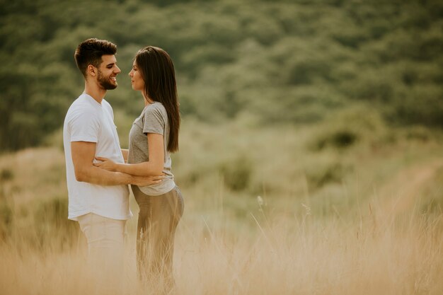 Giovani coppie felici nell'amore che cammina attraverso il campo di erba in una giornata estiva
