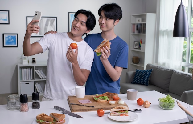 Giovani coppie gay asiatiche che sembrano felici mentre cucinano e prendono selfie Coppia di uomini LGBT che preparano insalata di pasti in cucina a casa