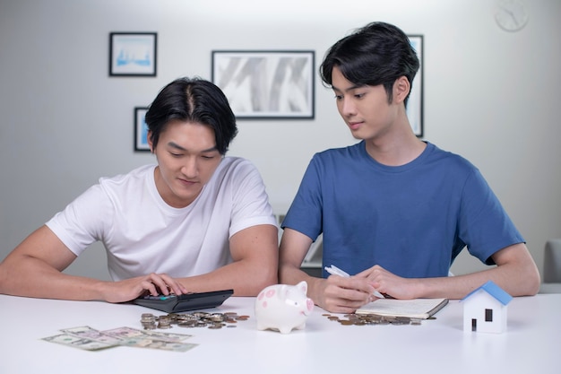 Giovani coppie gay asiatiche felici che risparmiano soldi per comprare una casa Coppie di uomini LGBT che risparmiano soldi per la famiglia e la casa