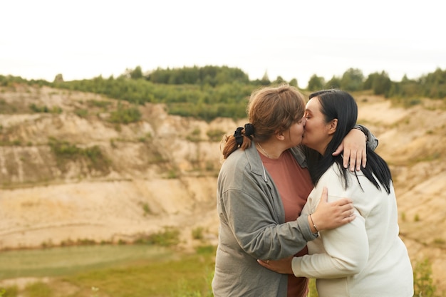 Giovani coppie lesbiche in sovrappeso che si abbracciano e si baciano all'aperto con splendida vista sullo sfondo