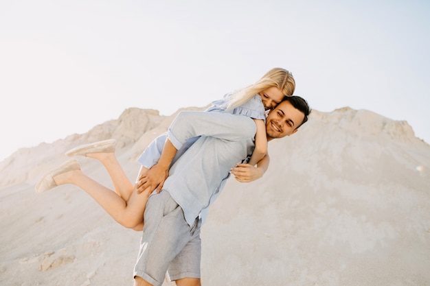 Giovani coppie romantiche all'aperto. Uomo che dà una cavalcatura sulle spalle, entrambi ridendo.